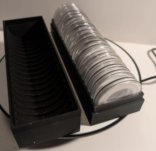Two open black 20-slot coin capsule storage boxes shown side by side, one loaded with capsules and one empty